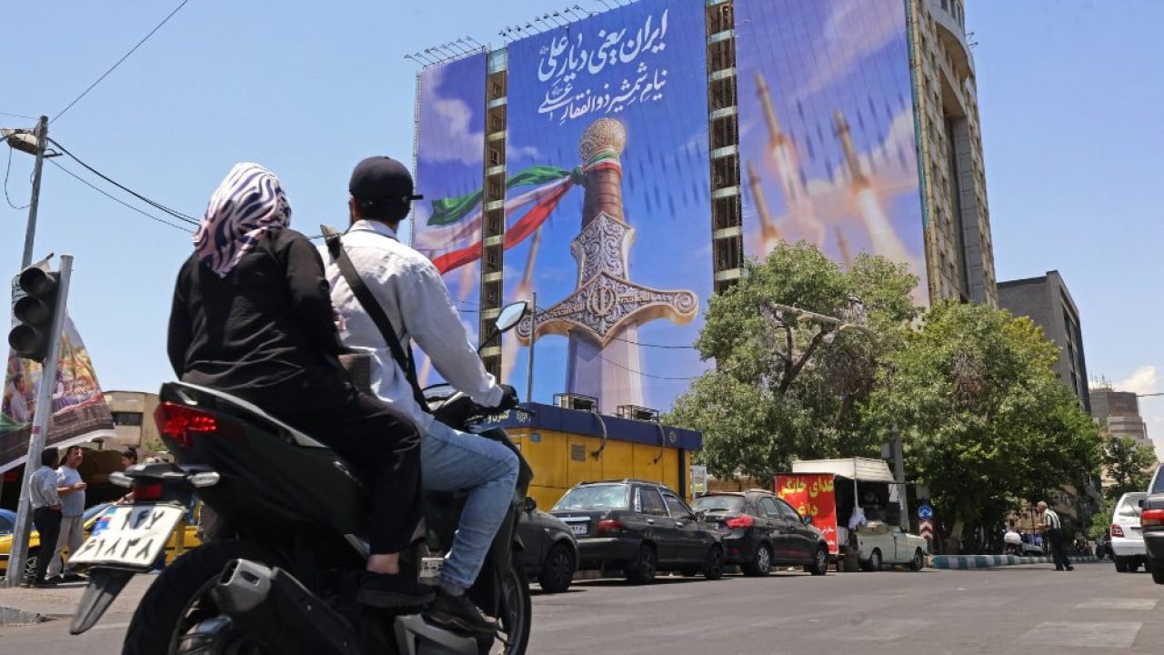 Foto: Motoristas passam por uma faixa gigante que retrata mísseis iranianos e um