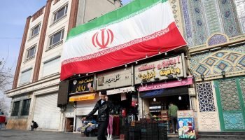 Foto: Um homem iraniano fala ao celular enquanto caminha ao lado de uma enorme b