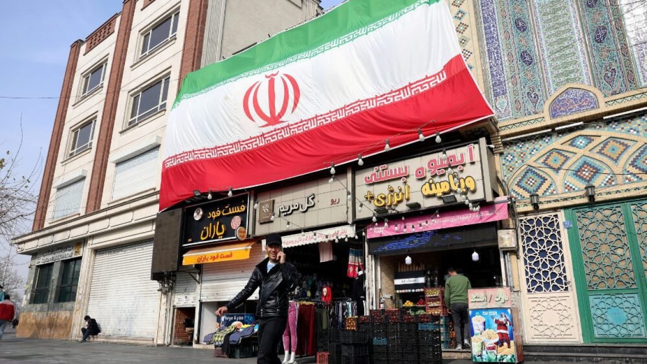 Foto: Um homem iraniano fala ao celular enquanto caminha ao lado de uma enorme b